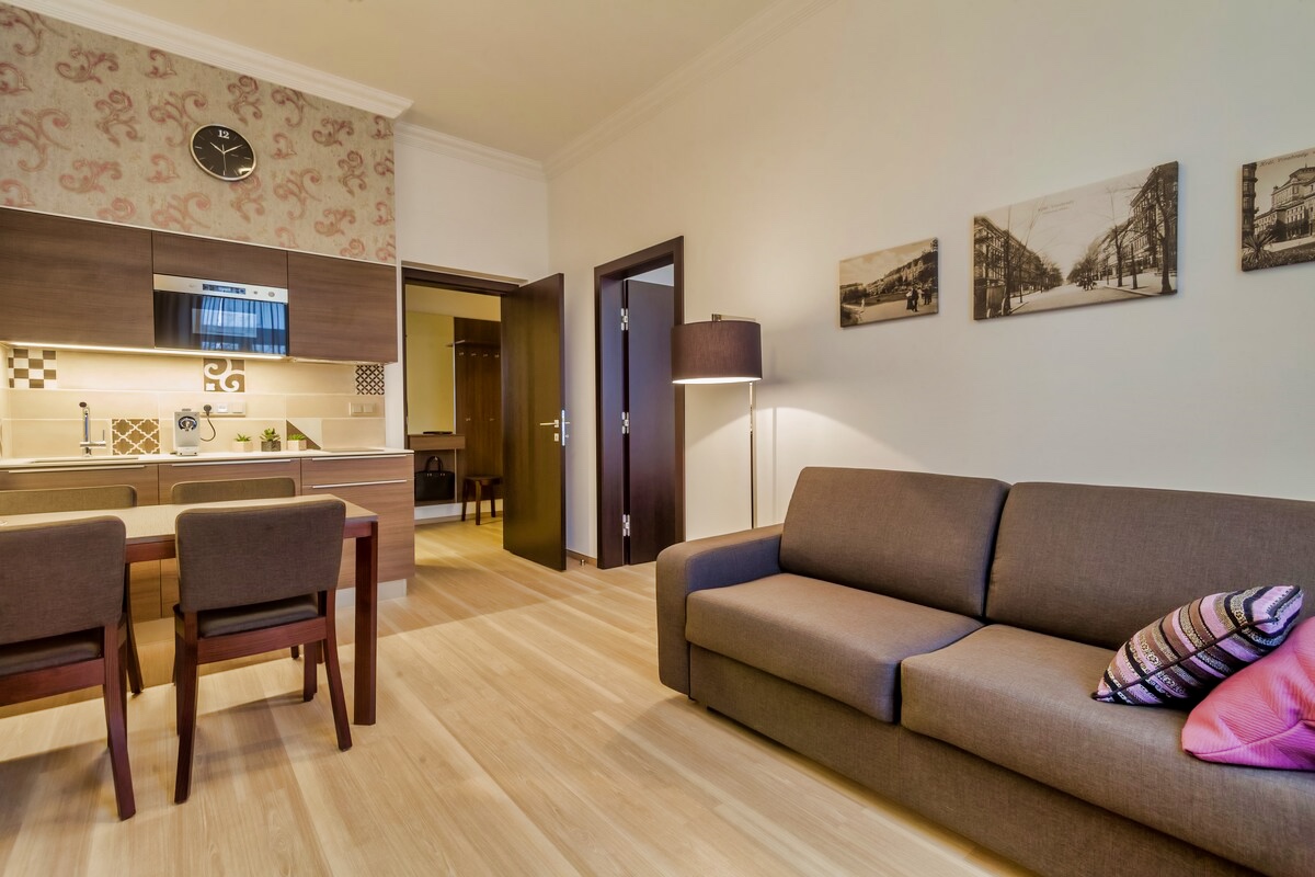 Experience comfort and style in our Deluxe Suite at Apartment Hotel Vinohradský Dům, Prague. Book now for a cozy living room with a couch, table, and chairs