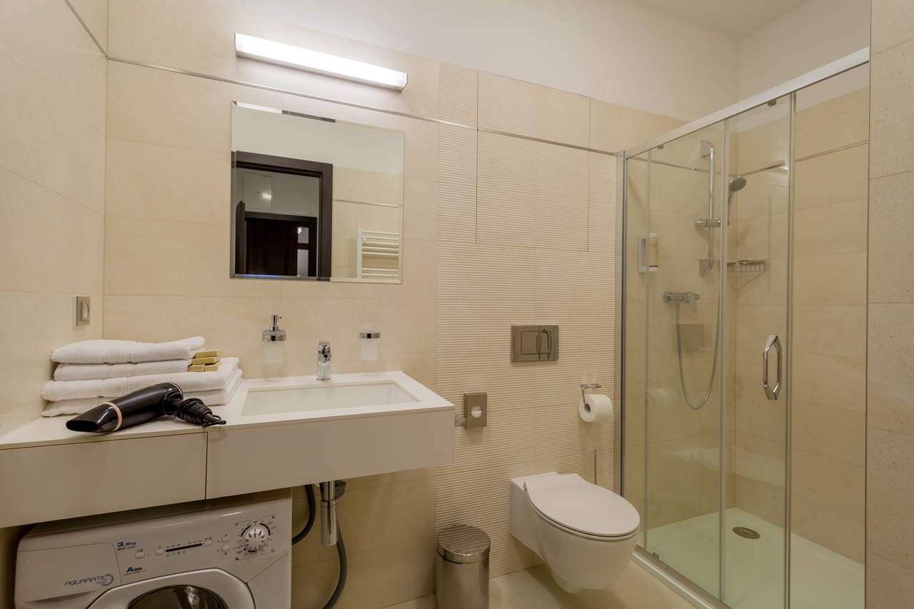 Discover the perfect blend of comfort and functionality in our bathroom at Aparthotel Vinohradský dům Prague - complete with a shower, toilet, and washing machine. Suite Deluxe.